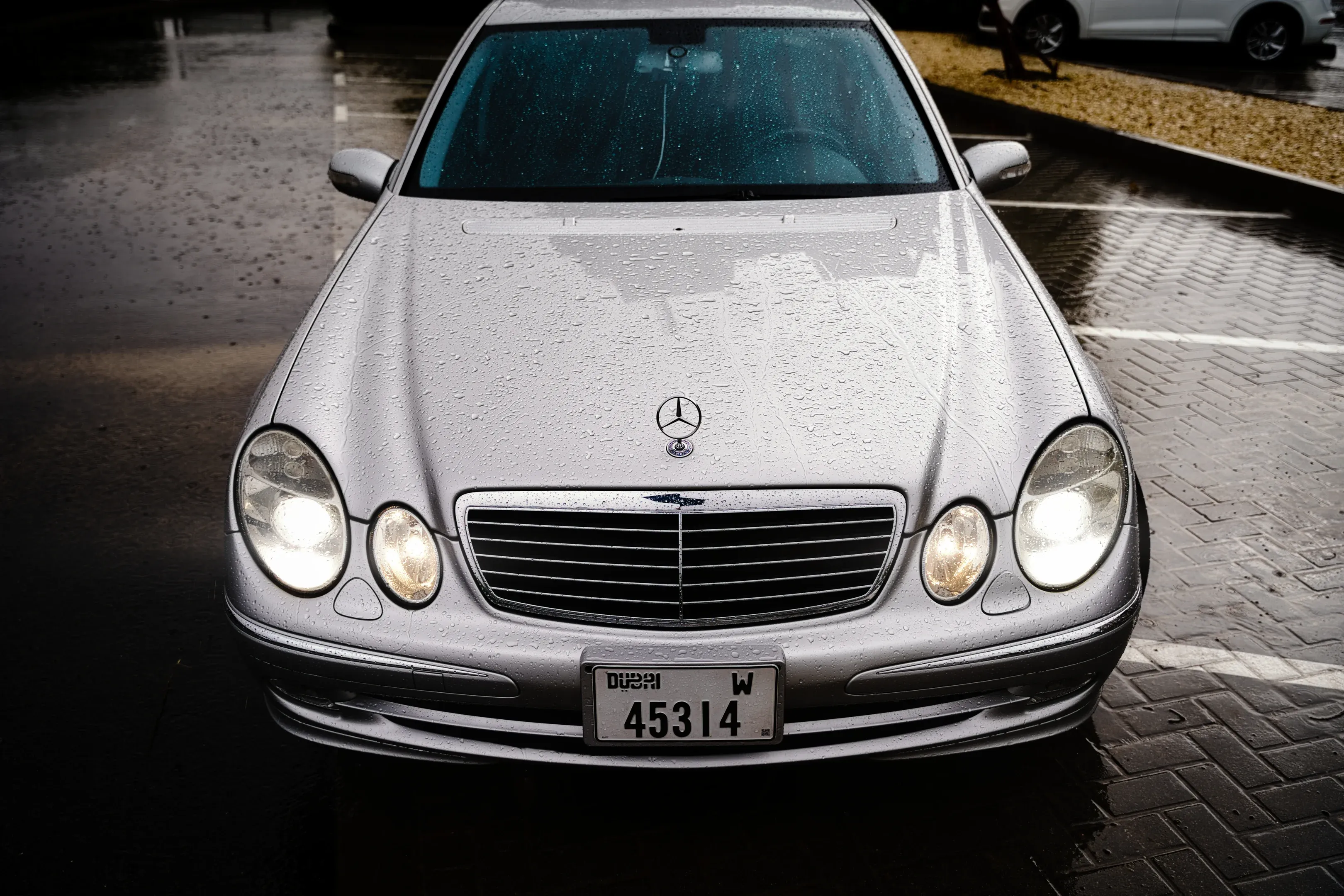 Rain-sculpted design: The classic quad-headlight face of the Mercedes W211 shimmering under a rare Dubai downpour.